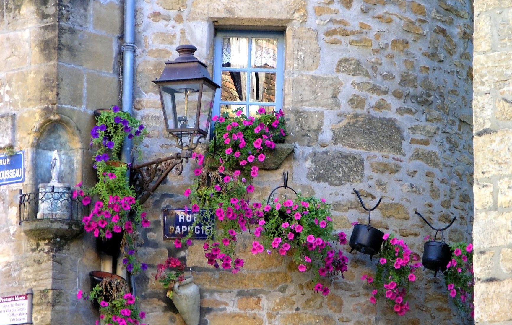 Stone wall adorned with vibrant pink petunias in Sarlat-la-Canéda, showcasing classic French architecture.